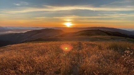 Wall Mural - Sunset view of the Santa Cruz mountains, with sun rays illuminating hills covered in dry grass; a layer of clouds visible in the background, covering the coastline; San Francisco Bay Area, California