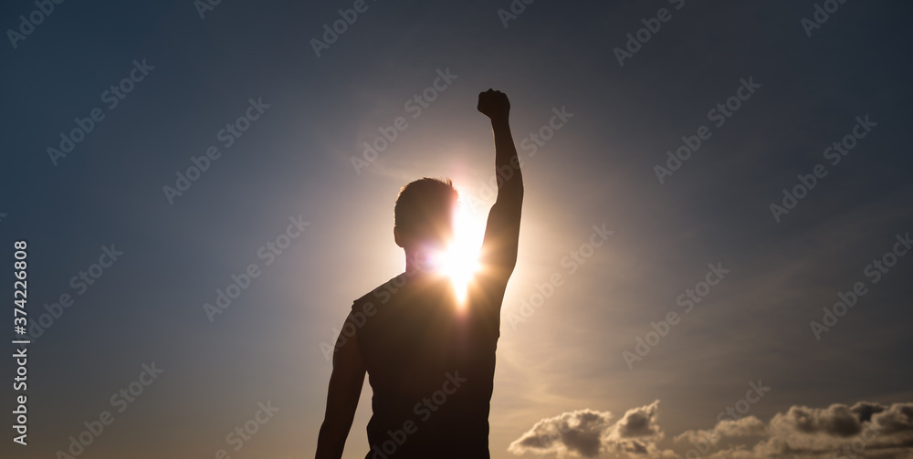 Young strong man with fist up to the sky feeling empowered, and determined.  - obrazy, fototapety, plakaty 