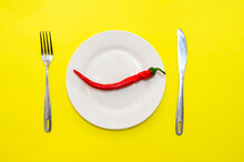 Red Chili Pepper On White Plate With Fork And Knife On Yellow Background Top View. Hot News Concept.