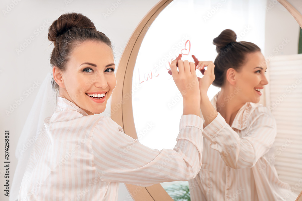 Beautiful young woman writing on mirror with lipstick