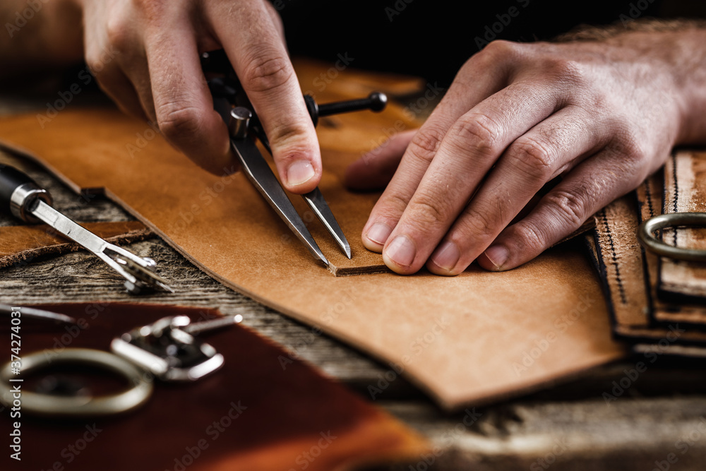 Close up of a shoemaker or artisan worker hands. Leather craft tools on old wood table. Leather craft workshop. - obrazy, fototapety, plakaty 