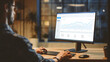 © Gorodenkoff - Over the Shoulder Confident Young Business Man Sitting at His Desk Using Desktop Computer with Statistics, Various Data, Charts and Graphs. Evening in Stylish Office Studio with City Window View