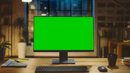 desktop computer with mock-up green screen standing on the wooden desk in the modern creative office