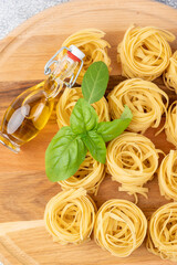 Uncooked dry tagliatelle pasta nest. On wooden board with basil and olive oil.