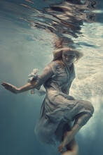 A Woman In A Blue Dress, Thin And Developing As In Weightlessness, Floats Under Water.