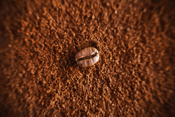 One roasted coffee bean, illuminated by light, lies on a crumbly ground coffee, which will make a strong invigorating drink.