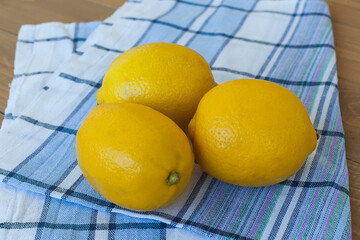 Three yellow lemons on a light checkered napkin. Three lemons on a wooden background.