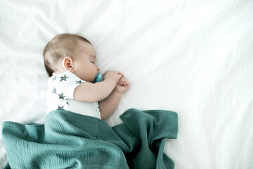 3 month old baby sleeping on bed and covered with a muslin diaper. Top view.