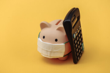 Wall Mural - Piggy bank with medical mask and calculator on yellow background. Economic disease. Financial crisis. Covid-19 pandemic