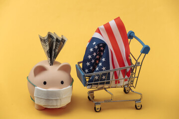 Wall Mural - Piggy bank with medical mask, Mini supermarket trolley with USA flag on a yellow background