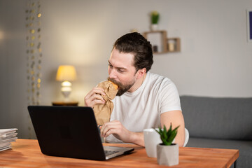 A young man works from home and eat food at desk with computer. Bad idea