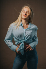 Wall Mural - Vertical shot of an attractive blonde female in jeans and a short shirt posing on a brown background