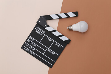 Wall Mural - Movie clapper board with light bulb on beige brown background. Filmmaking, Movie production, Entertainment industry. Top view