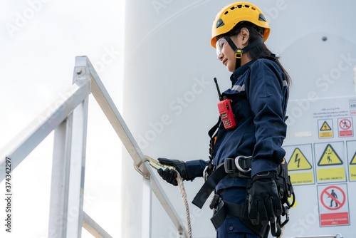 Asian woman Inspection engineer wearing safety harness and safety line working preparing and progress check of a wind turbine with safety in wind farm in Thailand.