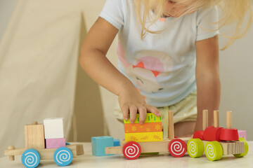 Toddler girl playing with wooden train made from wooden blocks - educational toys for preschool and kindergarten child. 