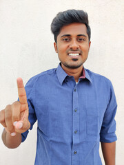 Wall Mural - Smiling south indian young man wearing blue shirt pointing up with fingers number one. Isolated on white background.