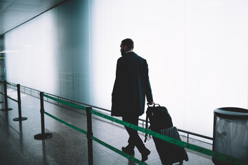 Faceless man with suitcase walking in airport corridor