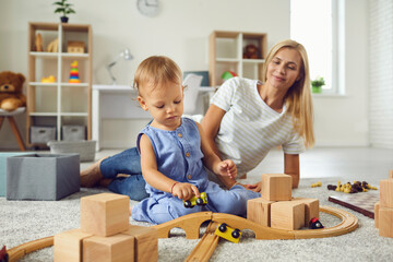 Wall Mural - Young babysitter and little child playing with wooden blocks in cozy nursery room