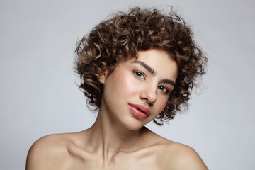 Portrait of beautiful young girl with curly hair and nude makeup