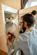 © Svitlana - Close up of young man, professional cook in apron taking ingredients out of the fridge while getting ready to prepare a meal, standing in the kitchen. Cooking at home concept