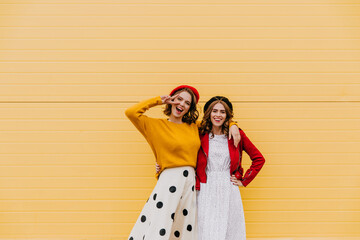 Sticker - Glad elegant girls standing near yellow wall. Outdoor shot of two french ladies.