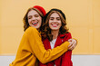 © Look! - Glad white woman with curly hairstyle embracing her brunette sister outdoor. Portrait of refined female models expressing happiness on yellow background.