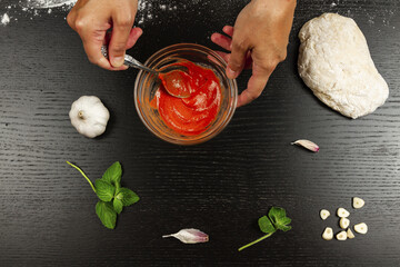 chef girl stirring tomato paste with cream, garlic and seasonings to make fresh italian homemade pizza