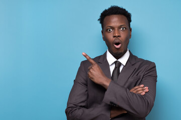 Canvas Print - Funny young african american man in suit pointing index fingers aside up.