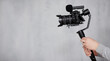 modern dslr camera on 3-axis gimbal stabilizer with follow focus system in male videographer hands over gray background