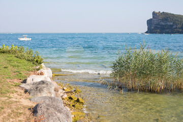 Landscape of the clear blue waters and grassy beach in San Biagio island, Manerba del Garda, Garda lake, Lombardy, Italy.