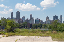Vacant Land On The Riverfront Of Astoria Queens New York With Overgrown Plants And A View Of The Roosevelt Island And Manhattan Skylines