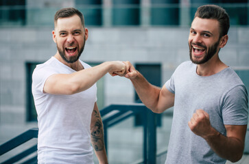 Two happy excited modern bearded best friends in casual clothes having fun and chatting together outdoors.