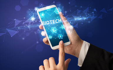 Female hand holding smartphone with BIOTECH inscription, modern technology concept