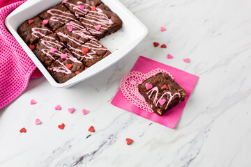 Wall Mural - Pan of Homemade Brownies with Pink Frosting on a White Countertop with Heart-Shaped Sprinkles; Piece on Pink Napkin and White Heart-Shaped Doily in Front with Heart-Shaped Sprinkles Scattered Around