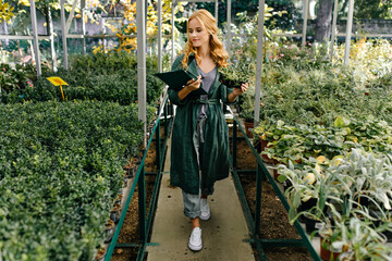 Wall Mural - Beautiful botanical garden, filled with many green flowers and bushes. Girl with blond curly hair, poses in front of camera, presenting herself as biologist