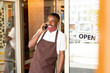 © pressmaster - Happy young waiter in uniform and protective mask standing in the door of cafe