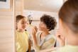 © pressmaster - Pretty young smiling woman touching face of her cute little daughter with brush