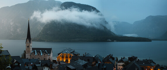 Wall Mural - Lake panorama view of the famous old town of Hallstatt with the idyllic place at night with lights on and low hanging foggy clouds in the mountains. Austrian Alps, Salzkammergut in Austria, Europe
