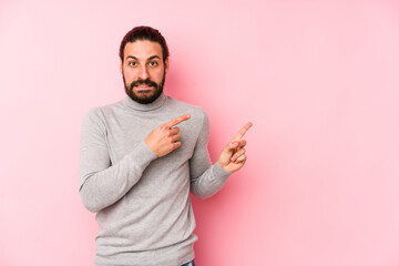 Wall Mural - Young long hair man isolated on a pink background shocked pointing with index fingers to a copy space.