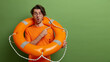 © wayhome.studio  - Emotional stunned man poses with safety equipment, uses lifebuoy on rescue, points at copy space, has shocked expression, isolated over green background. Time for swimming. Accident prevention