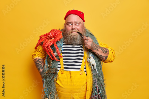 Fotomural Fishing lover caught octopus in sea or ocean, smokes pipe and thinks about future plans, has thick beard, spends almost all his life on boat