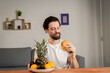 © Ivan - A young man sits at a table and talks about the usefulness of fruits, he picks them up and shows orange