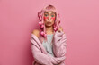Surprised Asian woman with pink hair, applies curlers, collagen patches during morning rush, undergoes beauty treatments, wears warm sweater, isolated on pink background. Cosmetic treatment.