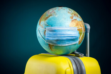 Wall Mural - Globe with medical face mask on luggage. Travel and coronavirus concept