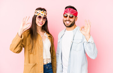 Wall Mural - Young caucasian couple wearing a music festival clothes isolated cheerful and confident showing ok gesture.