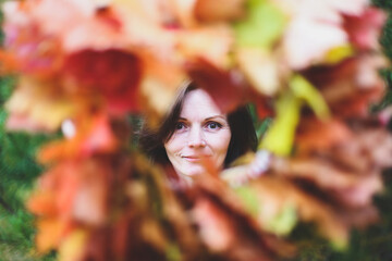 Brunette caucasian happy woman in circle frame of maple leaves wreath. Autumn harvest, nature concept. Flowers bouquet of orange, red, yellow leaves. Park, garden, forest fall photo shoot