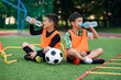 © gorynvd - Two teen boys in football uniforms having a rest on sport field with artificial covering and drinking fresh water.