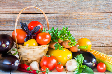 Wall Mural - Eggplant, tomatoes in a wicker basket, carrots and other vegetables on a wooden background