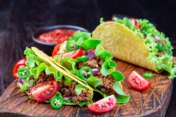 Wall Mural - Taco shells with ground beef meat, mashed avocado, tomato, lettuce, red onion and jalapeno pepper,  on wooden board, horizontal