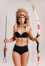 Girl In The Image Of Indigenous Peoples Of America With A Bow And Arrow Posing On A Light Background